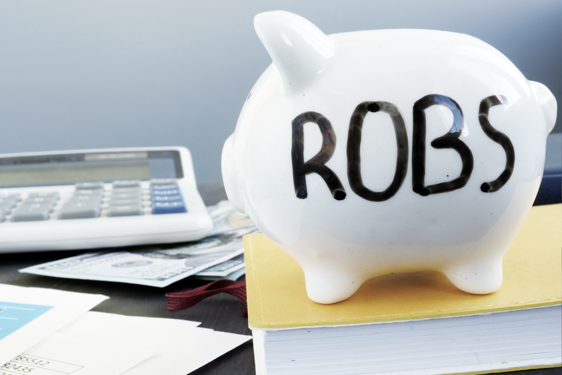 ROBS 401k business financing piggy bank on desk with paperwork and calculator.