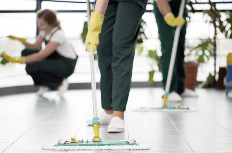 Three people mop the floor and wipe window panes down wearing yellow gloves and uniforms - Cleaning services is an industry that's proven to be recession proof. 