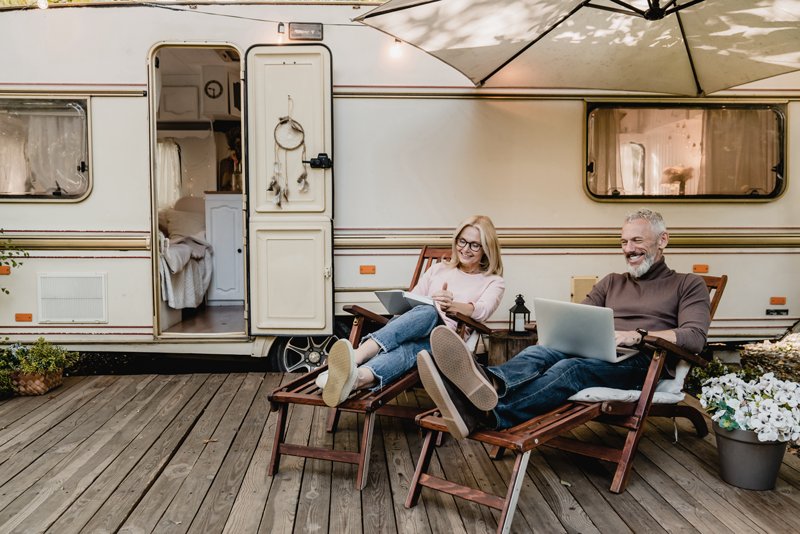A couple sits outside an RV together, working on their devices - Budget travel is a recession proof industry, especially now. 