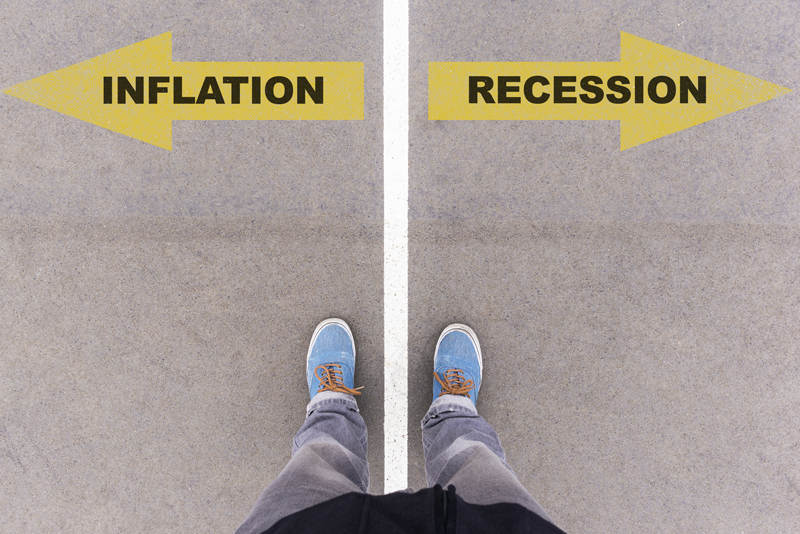 Image of a person standing in-between a road with an arrow reading "inflation" at one end and "recession" at the other end. 
