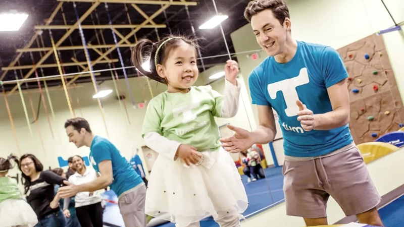 Tumbles is one of the top childcare franchises of 2022, offering a unique STEAM program. Image shows Tumbles employees working with younger children in a vibrant Tumbles environment. 