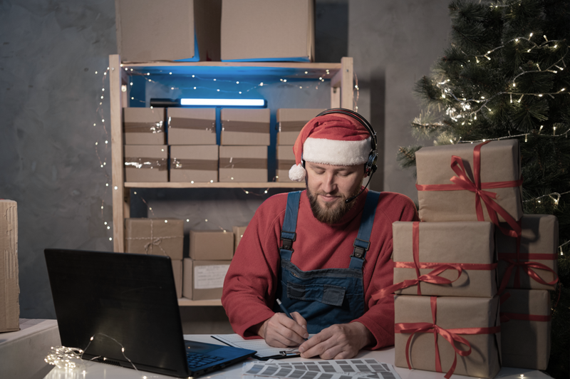 Business owner managing holiday stress and business owner stress, working at a desk with gift boxes and paperwork. 
