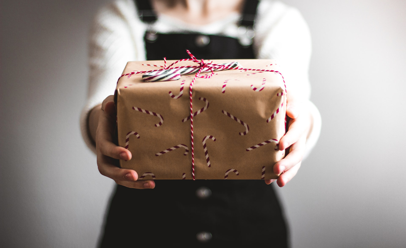 A woman holding a wrapped holiday present with a candy-cane on top. Hosting events, contests, or giveaways can help increase holiday sales. 
