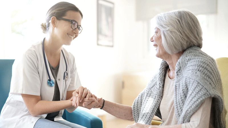 Healthcare professional wearing a medical jacket holds an older woman's hand - Photo for top senior and medical franchises of 2022.