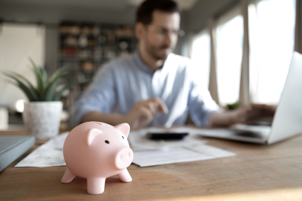 How To Pay Yourself as a Business Owner with ROBS - Man calculating money at his desk with a piggy bank in focus. 