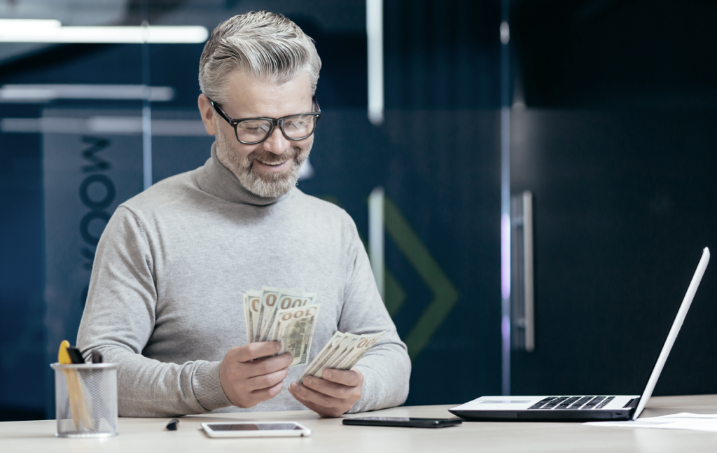 Older man counting money at his office desk (How To Pay Yourself as a Business Owner). 