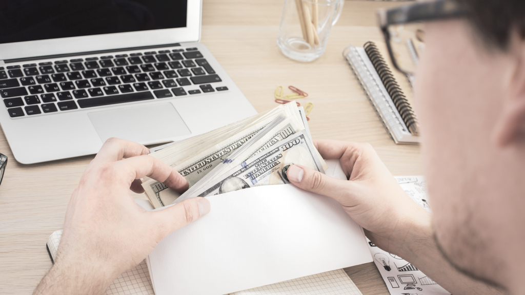 Man counting money from envelope at desk (How To Pay Yourself as a Business Owner). 