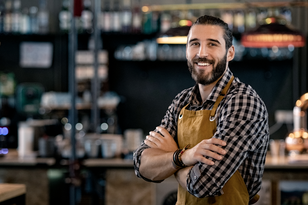 A business owner man in a cafe looking confident and posed with his arms crossed. (How to Navigate Business Uncertainty - Blog). 
