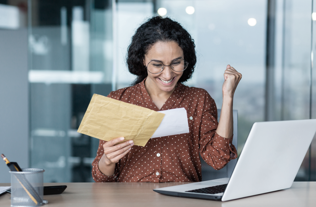 Woman sitting at her desk looks excited as she opens a letter. (Business Grants for Women Blog - Guidant). 