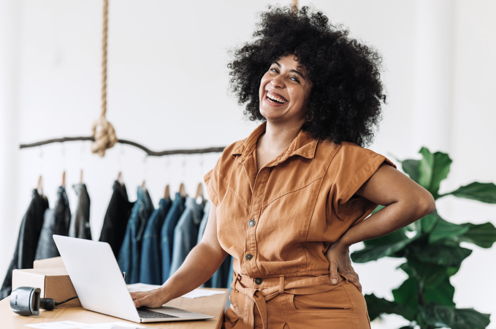 Woman smiling at her laptop with business items in the background. (Business Grants for Women Blog - Guidant). 