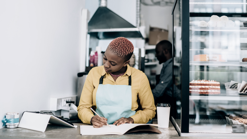 Black woman business owner filling out paperwork at her cafe business. (Blog: Small Business Week, Big Dreams: How to Find and Secure Business Financing)