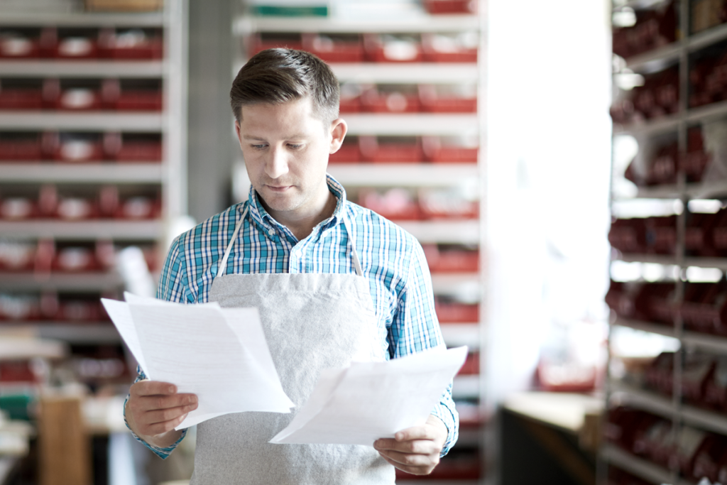 Small business owner comparing two sheets of paper in his shop. (10 Tax Benefits of C Corporations - Guidant Blog.)