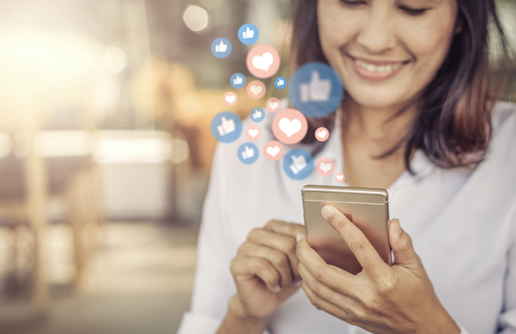Woman on her phone with likes and heart icons floating above it (Ways to Celebrate Small Business Week - Guidant Blog)