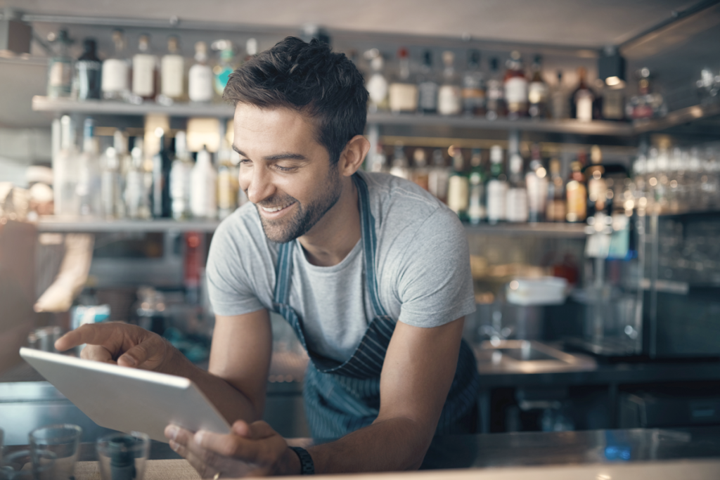 Male business owner at a restaurant smiling while looking at his tablet. (Top Franchise Industries and Industry Trends - Guidant Financial Blog.)