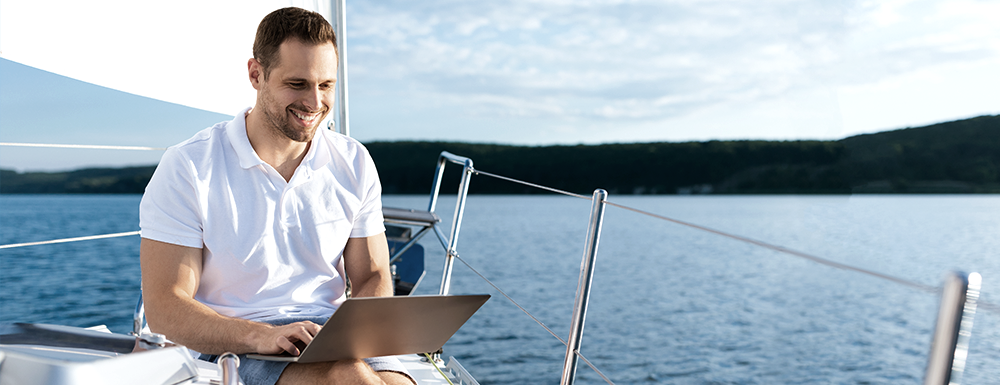 Summer Travel Planning Tips and Guide from Guidant (Photo header of a man on his laptop while sailing).