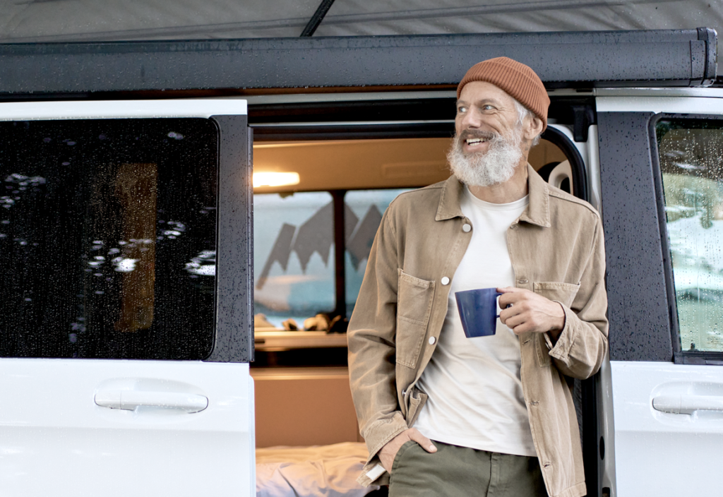 Older man holding a mug outside of a van while traveling, smiling and looking into the distance.  (Tips on How to Run Your Small Business on Summer Vacation - Guidant Blog.)