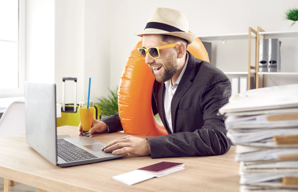 White man wearing sunglasses and a business suit, smiling at desk with a summer themed drink and floaty around his arm and a sun hat. (Turn Up the Heat with these Top 7 Summer Sale Promotion Ideas for Small Businesses - Guidant Blog.)