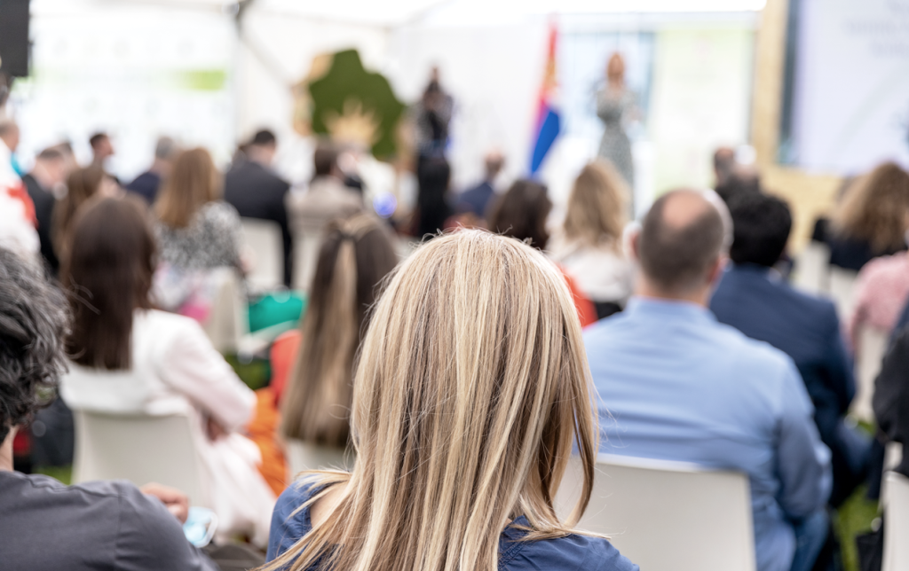 A photo of a crowd of people attending an event with a speaker. (Top 5 Best Upcoming Entrepreneur Events - Guidant Blog).