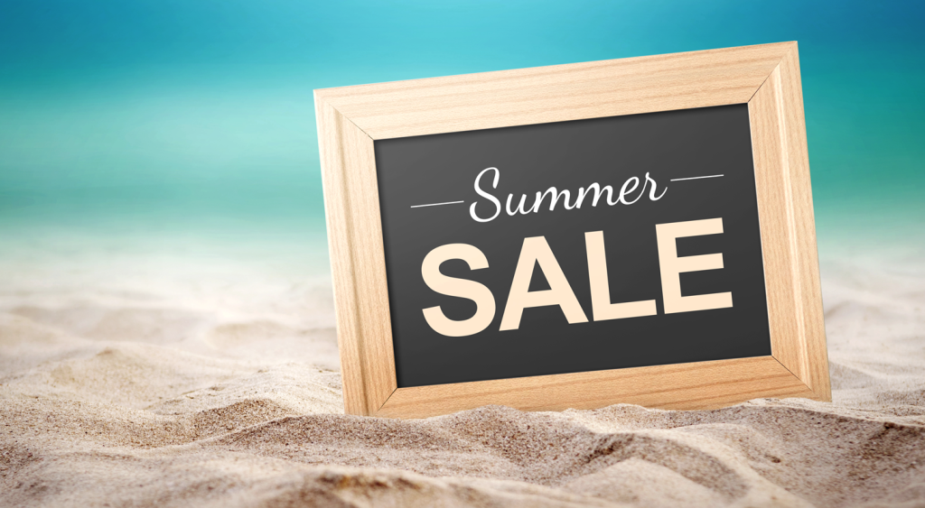 Chalkboard sign sitting on the sand with a blue background, reading "Summer Sale." (Turn Up the Heat with these Top 7 Summer Sale Promotion Ideas for Small Businesses - Guidant Blog.)