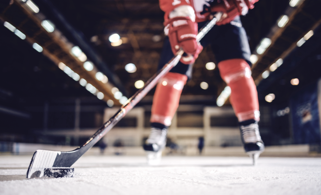 Hockey player holding a hockey stick on the ice with a puck. (Boost Your Small Business with the Power of Hockey Stick Growth in 7 Steps - Guidant).