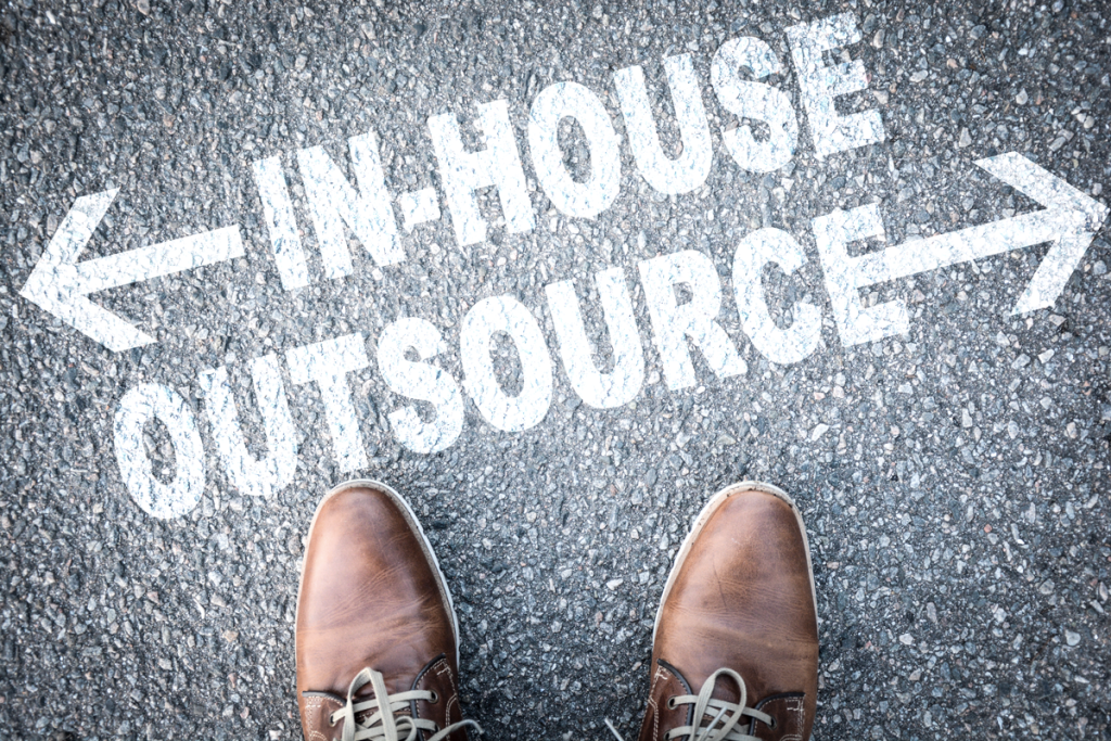 Shoes on a road pointing at text with arrows, one pointing left with "In-House" and another right with "Outsource." (Top 5 Surprising Benefits of Offshoring for Small Businesses - Guidant)