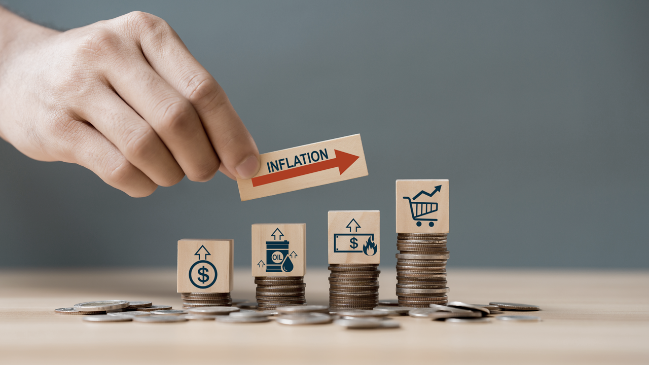 Hand holding a block that reads "Inflation" with a red arrow pointing upward. Below are other blocks on stacks of US coins with money and shopping symbols. (Inflation-Proofing Your Small Business: Insights and Tactics from Successful US Entrepreneurs - Guidant Blog).