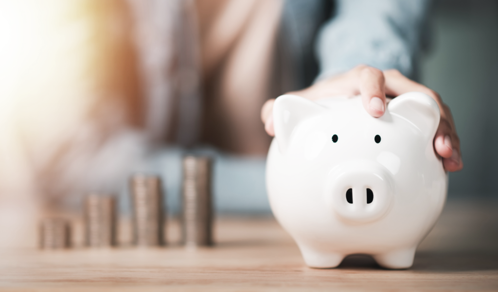 Person in background holding a piggy bank with stacks of coins on table. (7 Best Options for Small Business Funding - Guidant Blog). 