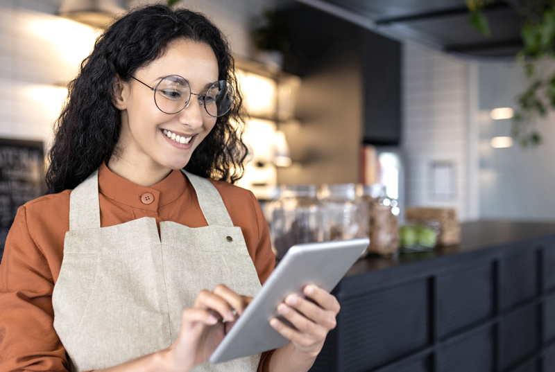 Woman business owner holding a tablet and smiling inside store. (Top Resources and Grants for Hispanic Entrepreneurs - Guidant Financial Blog).