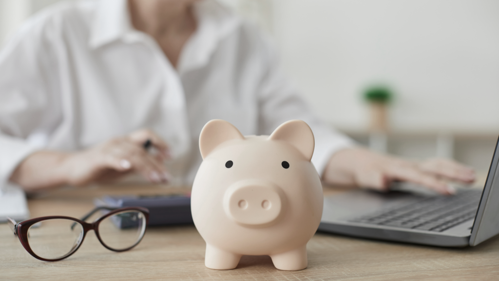 Piggy bank on desk next to glasses and a laptop. (Demystifying Top Heavy 401k Plans: What You Need to Know - Guidant Blog.)
