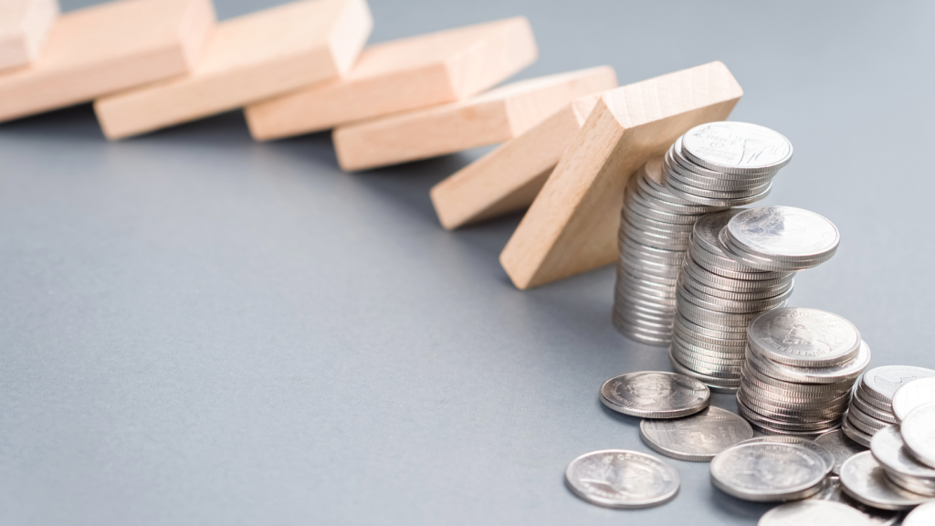 Dominoes falling down onto coins. (Navigating the New Banking Landscape as a Small Business - Guidant Blog).