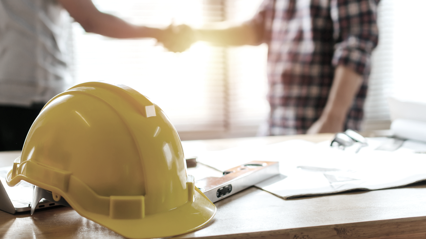 Contractor construction hat in the fore with two men shaking hands in the background. (Complete Guide to Payroll for Small Businesses - Guidant Financial.)