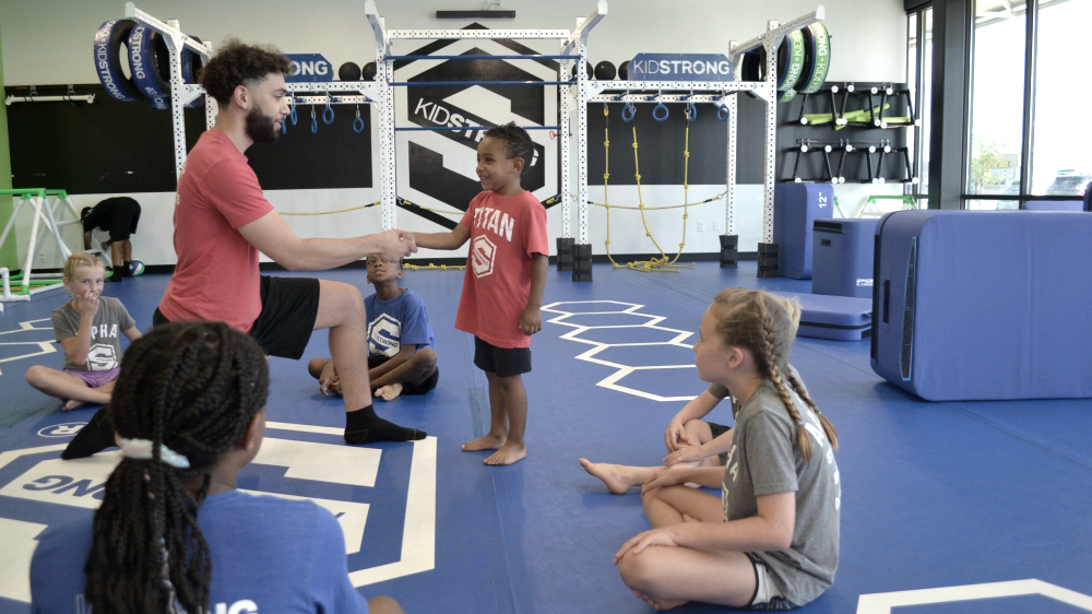 Coach shaking hands with a child in a KidStrong gym. Photo from KidStrong. (Hottest Fitness Franchises of 2023-2024 - Guidant Blog).