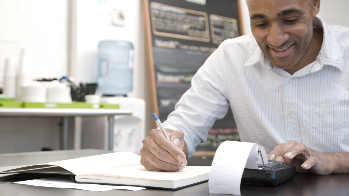 Man at desk with a calculator smiling. (Complete Guide to Payroll for Small Businesses - Guidant Financial.)