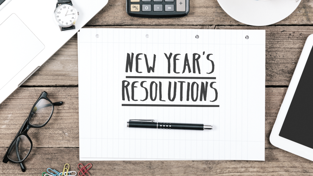 "New Year's Resolutions" written on a notepad with a pen on a desk landscape. (Top 5 Must-Have New Year's Resolutions for Your Small Business - Guidant Blog.)