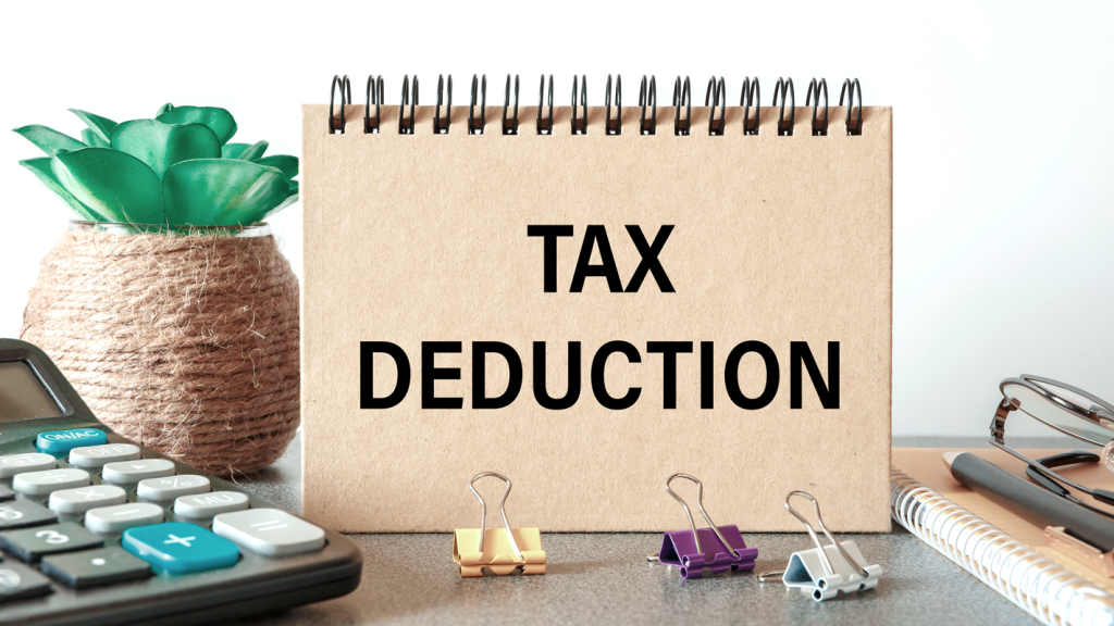 Notebook reading "Tax Deduction" on a desk with a calculator and other desk accessories. (From Deductions to Deadlines: Your Guide to Mastering Taxes for Small Businesses - Guidant Blog).