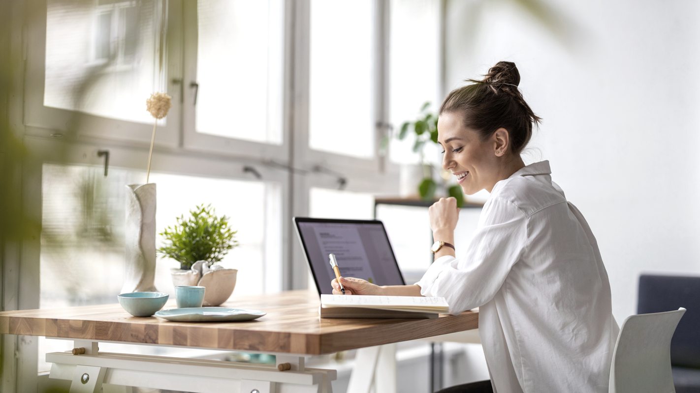 Woman smiling while completing work at a desk. (Complete Guide to Payroll for Small Businesses - Guidant Financial.)