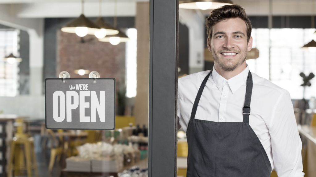 Smiling business owner next to an open sign. (How to Find Your Business Niche - Guidant Blog).