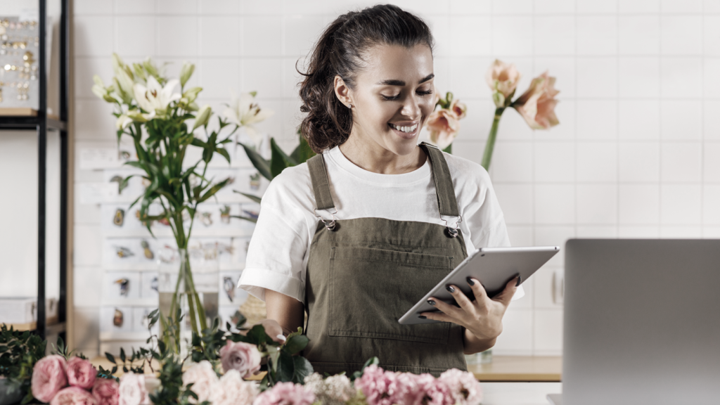 Smiling woman business owner holding a tablet next to floral arrangements. (What You Need to Start a Business in 2024 - Starting a Business, Guidant Blog)