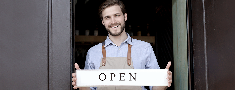 Happy business owner holding an open sign. (What You Need to Start a Business in 2024 - Guidant Blog)
