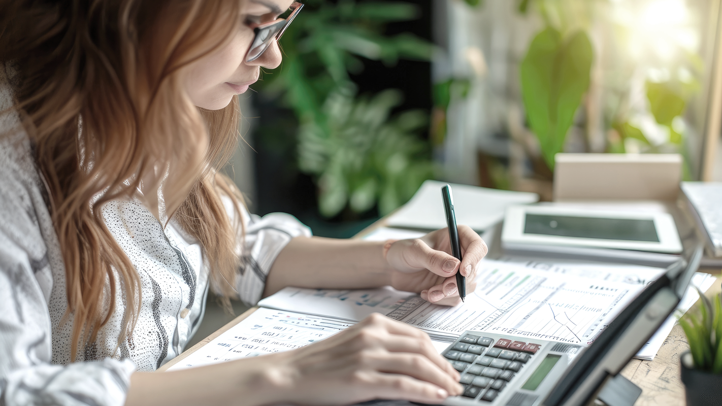 Woman doing accounting paperwork on desk. (Complete Guide to Bookkeeping - Guidant Financial).