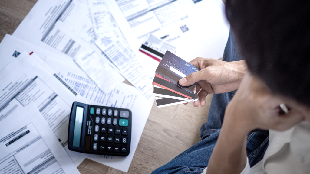 Person holding credit cards looking at piles of bills and a calculator. (7 Common Business Pitfalls and How to Avoid Them - article by Jeremy Ames).