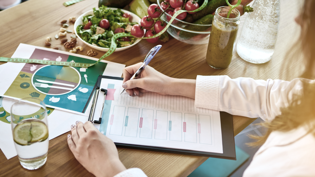 Person filling out paperwork next to vegetables and a nutrition plan. (7 Creative Health and Wellness Business Ideas - Guidant Blog)