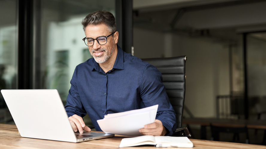Business man working at desk smiling. (More than Financials: What to Look for When Buying a Business - Article by Jeremy Ames, CEO and Co-Founder of Guidant Financial)