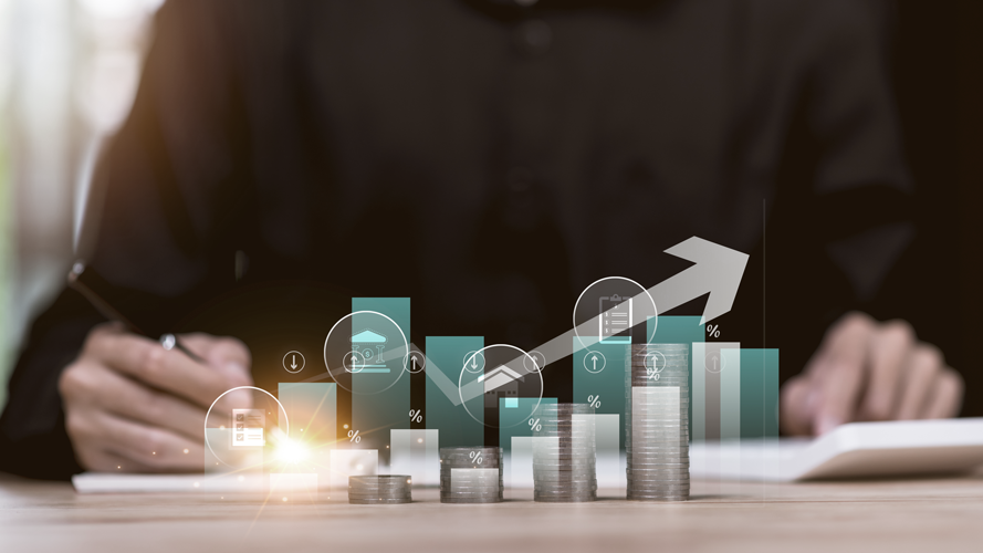 Person at desk with coins and graphics showing growth. (How to Create a Winning Business Financial Strategic Plan - Guidant blog). 