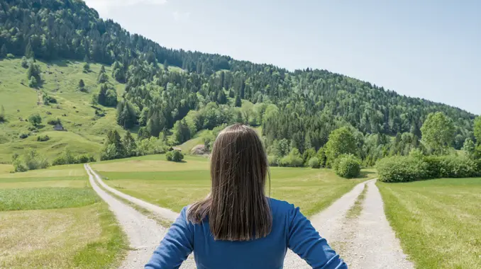 Woman with her back toward the camera looking down two paths. Franchising vs Starting a Business From Scratch vs Buying an Existing Business: Which One is Right for You? - Guidant Blog.